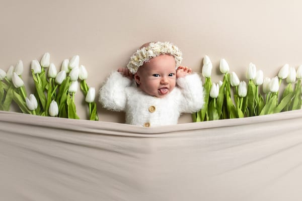 Baby mit Blütenkranz streckt die Zunge heraus, umgeben von weißen Tulpen