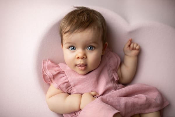 Baby im rosa Rüschenkleid liegt in einer herzförmigen Mulde