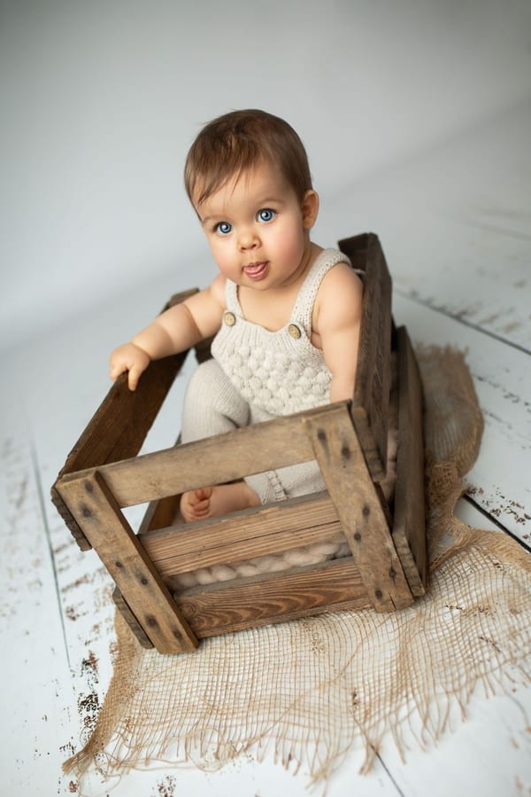 Baby sitzt in einer Holzkiste und streckt frech die Zunge heraus