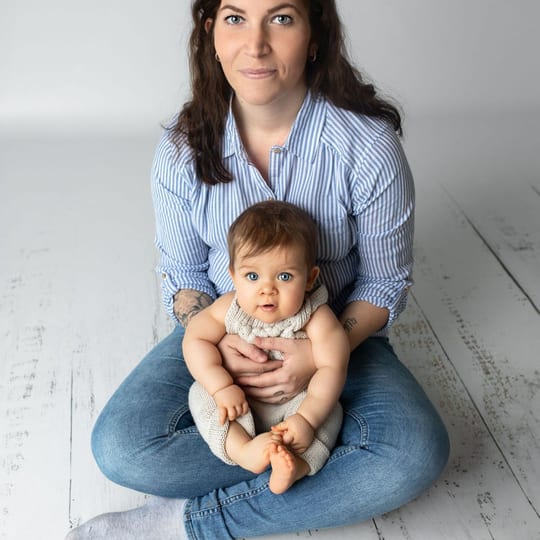 Mutter sitzt im Schneidersitz auf dem Boden, ihr Baby sitzt sicher zwischen ihren Beinen