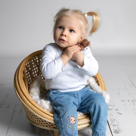 Kleines Mädchen mit Zöpfchen sitzt in einem Rattansessel und faltet die Händchen