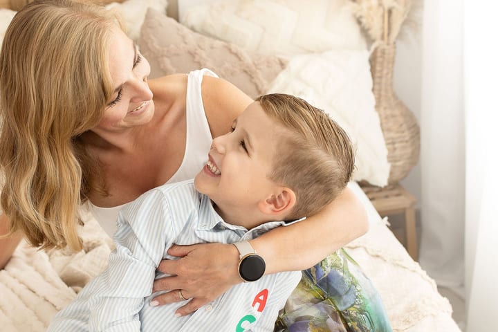 Mutter umarmt ihren lachenden Sohn auf dem Bett, beide schauen sich an