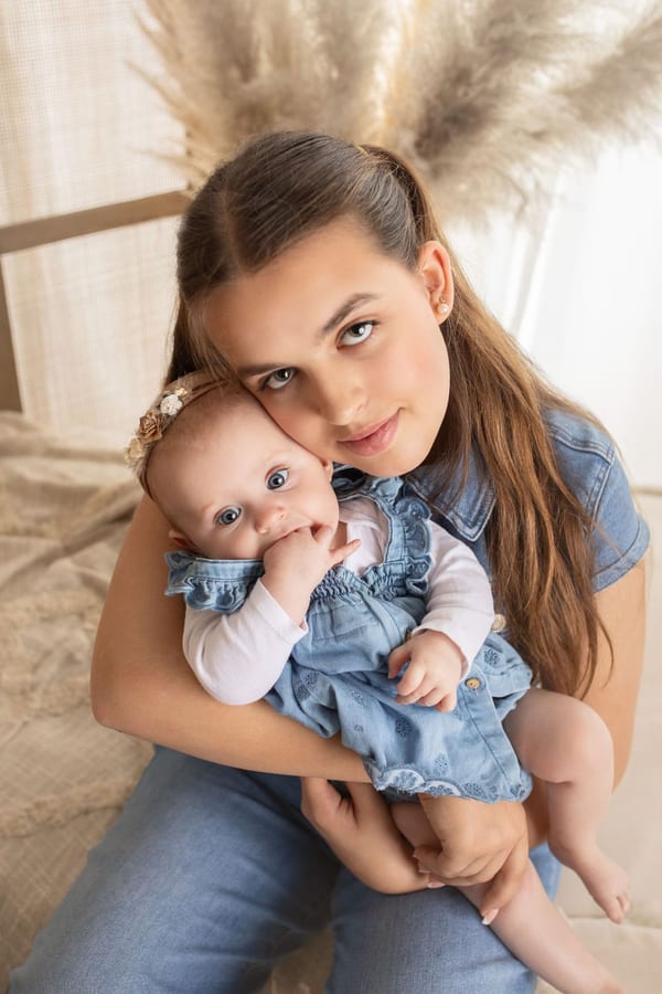 Große Schwester hält ihre kleine Schwester im Jeanskleid im Arm