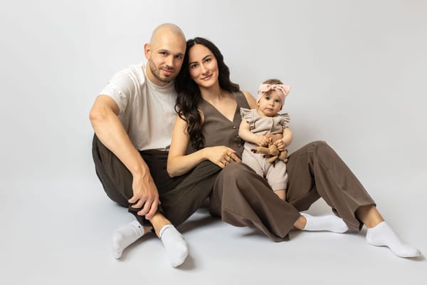 Eltern sitzen entspannt auf dem Boden, die kleine Tochter mit Schleife sitzt dicht bei Mama