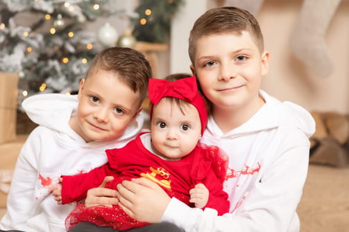 Zwei große Brüder halten ihre kleine Schwester im roten Kleid mit Haarschleife