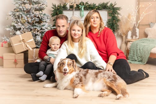 Familie mit zwei Kindern und Australian Shepherd auf dem Studioboden zwischen Geschenken