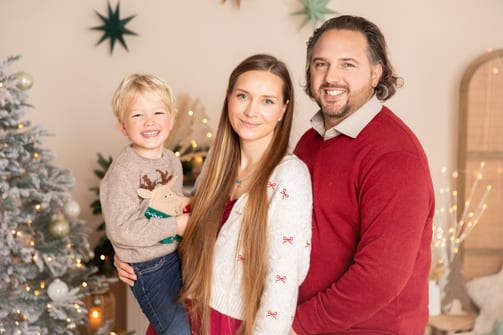Mutter und Vater mit ihrem Sohn im Rentier-Pulli vor dem Tannenbaum