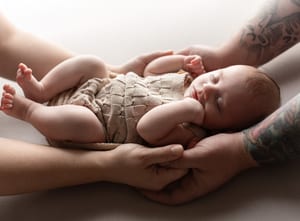 Elternhände halten ein schlafendes Neugeborenes im Strickhöschen