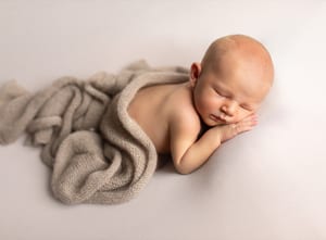 Neugeborenes schläft auf dem Bauch, halb zugedeckt mit einer Strickdecke