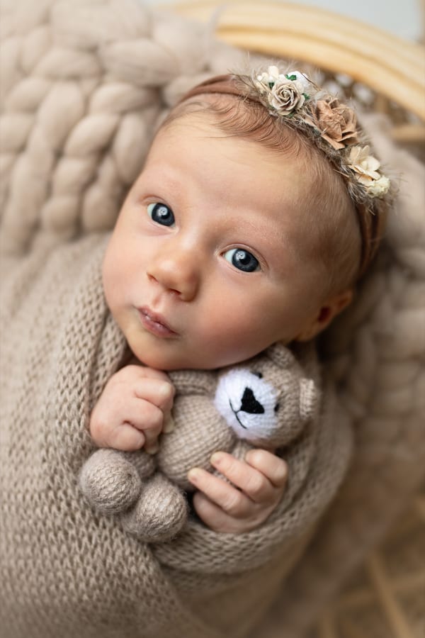 Waches Neugeborenes mit Blütenhaarband hält einen Strickteddy
