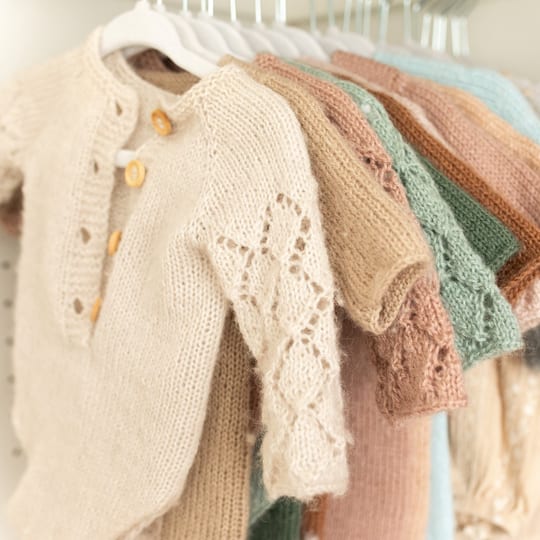 Zarte Strickoutfits für Neugeborene an der Kleiderstange im Atelier